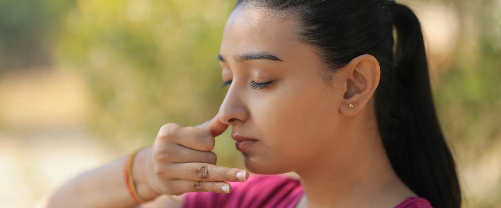 A woman with her eyes closed practising alternate-nostril breathing outdoors