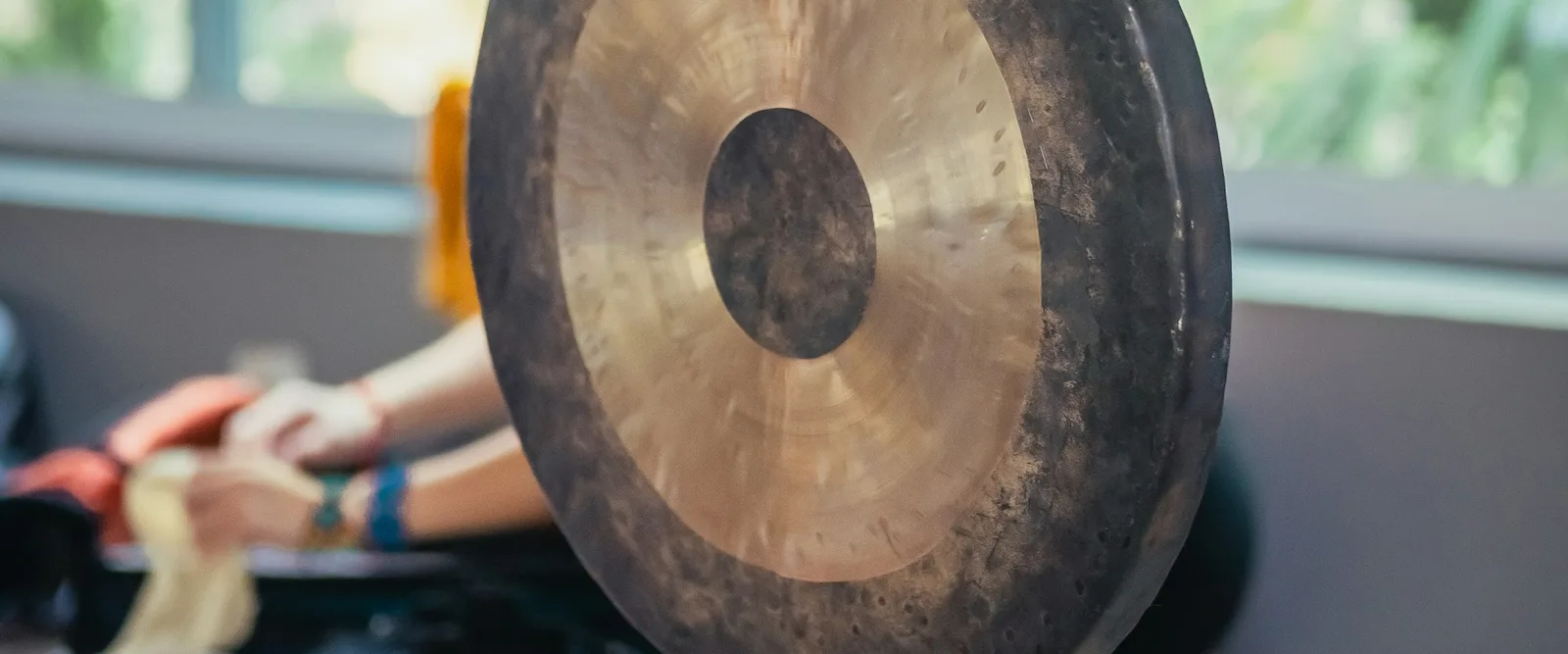 A large gong on its stand, with the practitioner and their bowls on the floor behind it