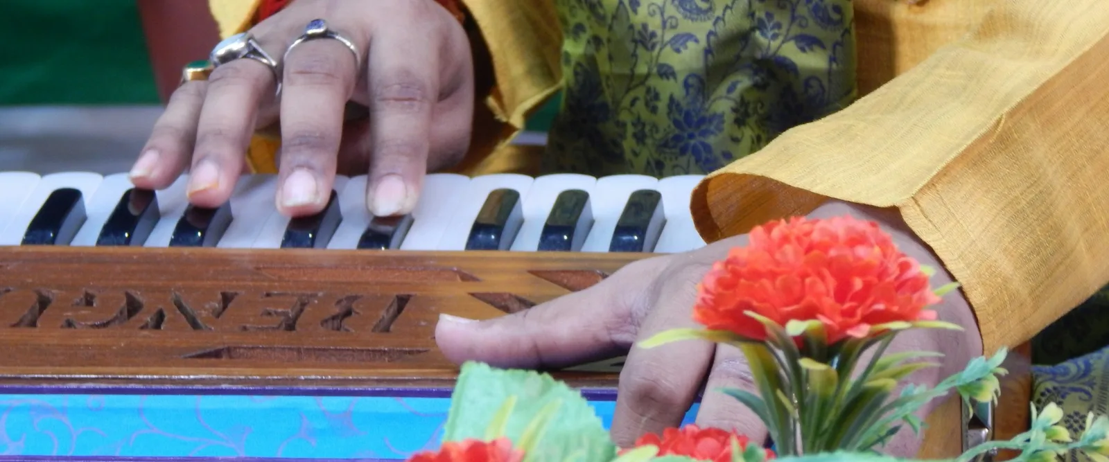 Hands playing a harmonium, with marigolds set beside the keys