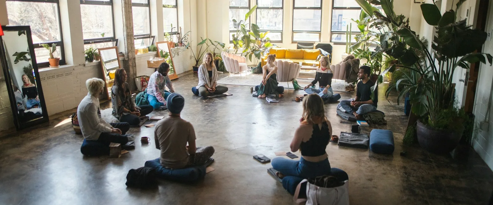 A group sitting on cushions in a circle in a bright plant-filled room