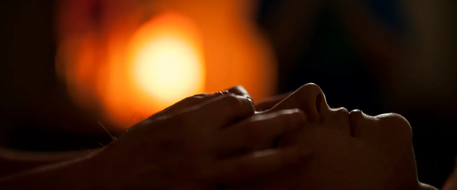A practitioner's hands resting on someone's head by candlelight