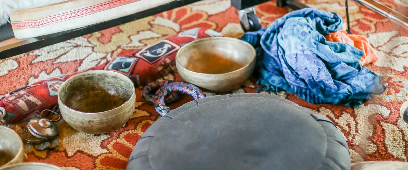 Singing bowls, cushions and a gong laid out on a patterned rug before a sound bath